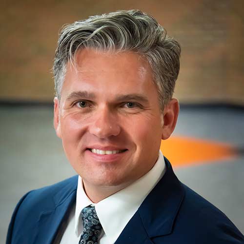 a man wearing a suit and tie smiling at the camera