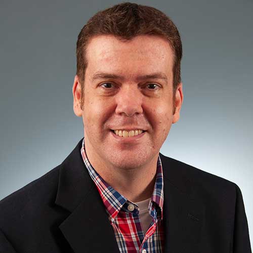 a man wearing a suit and tie smiling at the camera