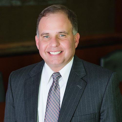 a man wearing a suit and tie smiling at the camera