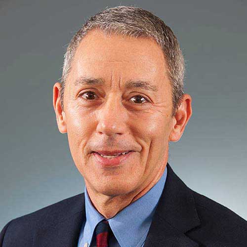 a man wearing a suit and tie smiling at the camera