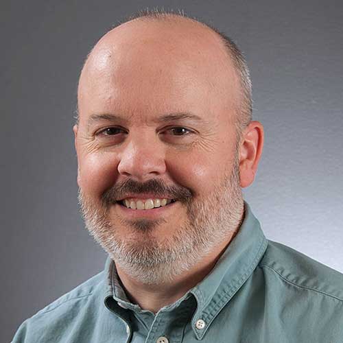 a man wearing glasses and smiling at the camera