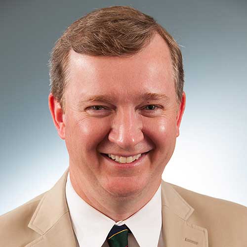 a man wearing a suit and tie smiling at the camera