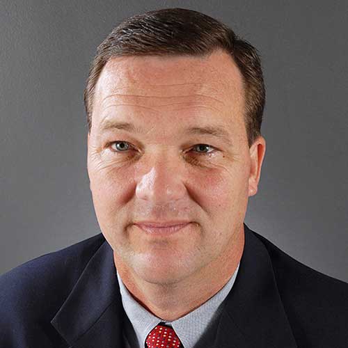 a man wearing a suit and tie smiling and looking at the camera