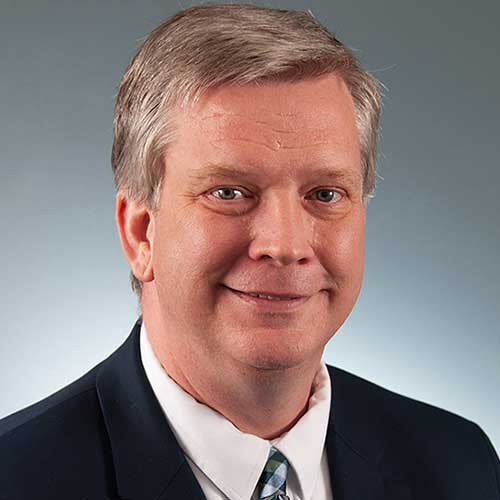 a man wearing a suit and tie smiling at the camera