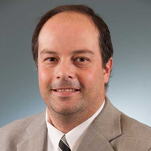 a man wearing a suit and tie smiling at the camera