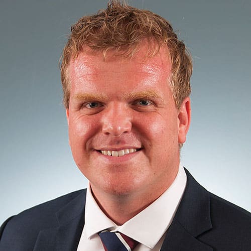a man wearing a suit and tie smiling at the camera