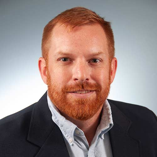 a man wearing a suit and tie smiling and looking at the camera