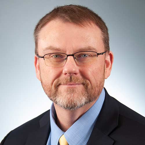 Derrick Smith wearing a suit and tie smiling and looking at the camera
